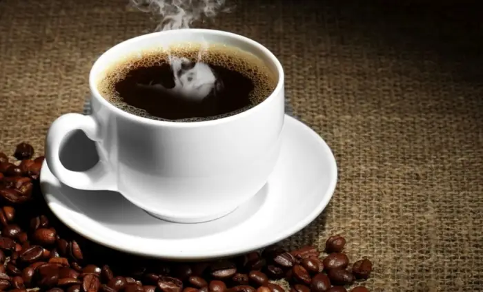 O ceașcă cu cafea aburindă alături de boabe intregi de cafea