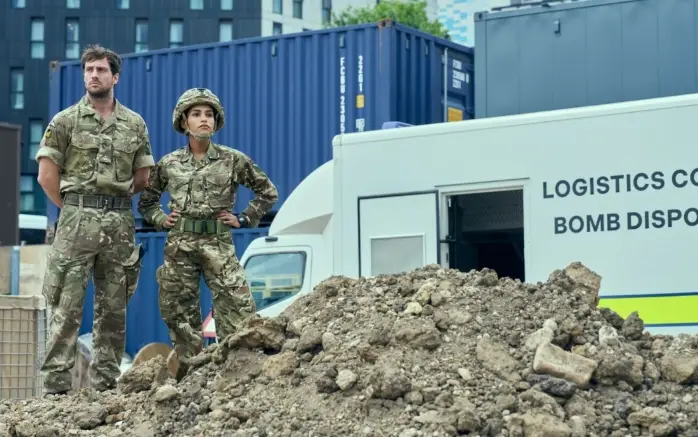 Echipa de deminare în filmul Fuze (2025) Doi militari în uniformă de camuflaj pe moloz, în fața unui vehicul de deminare – scenă din thrillerul Fuze (2025), regia David Mackenzie