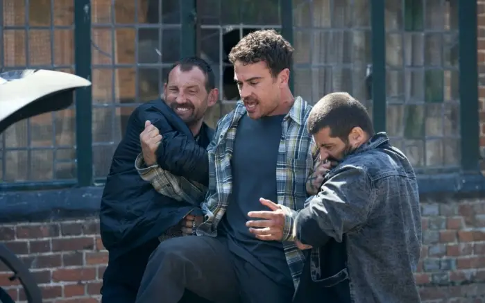 Theo James în rolul lui Karalis în Fuze (2025) Theo James (centru) în rolul liderului de bandă Karalis, flancat de doi complici – scenă de acțiune din filmul Fuze (2025)