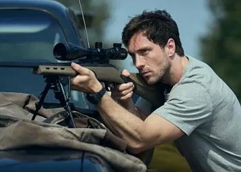 Actor cu pușcă cu lunetă poziționat &icirc;n spatele unui autoturism, scenă de suspans din filmul Fuze (2025) cu Aaron Taylor-Johnson